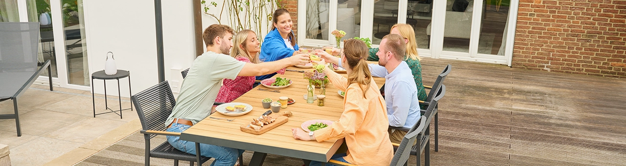 Ein Tisch aus Teakholz, an dem Leute sitzen und gemeinsam anstoßen